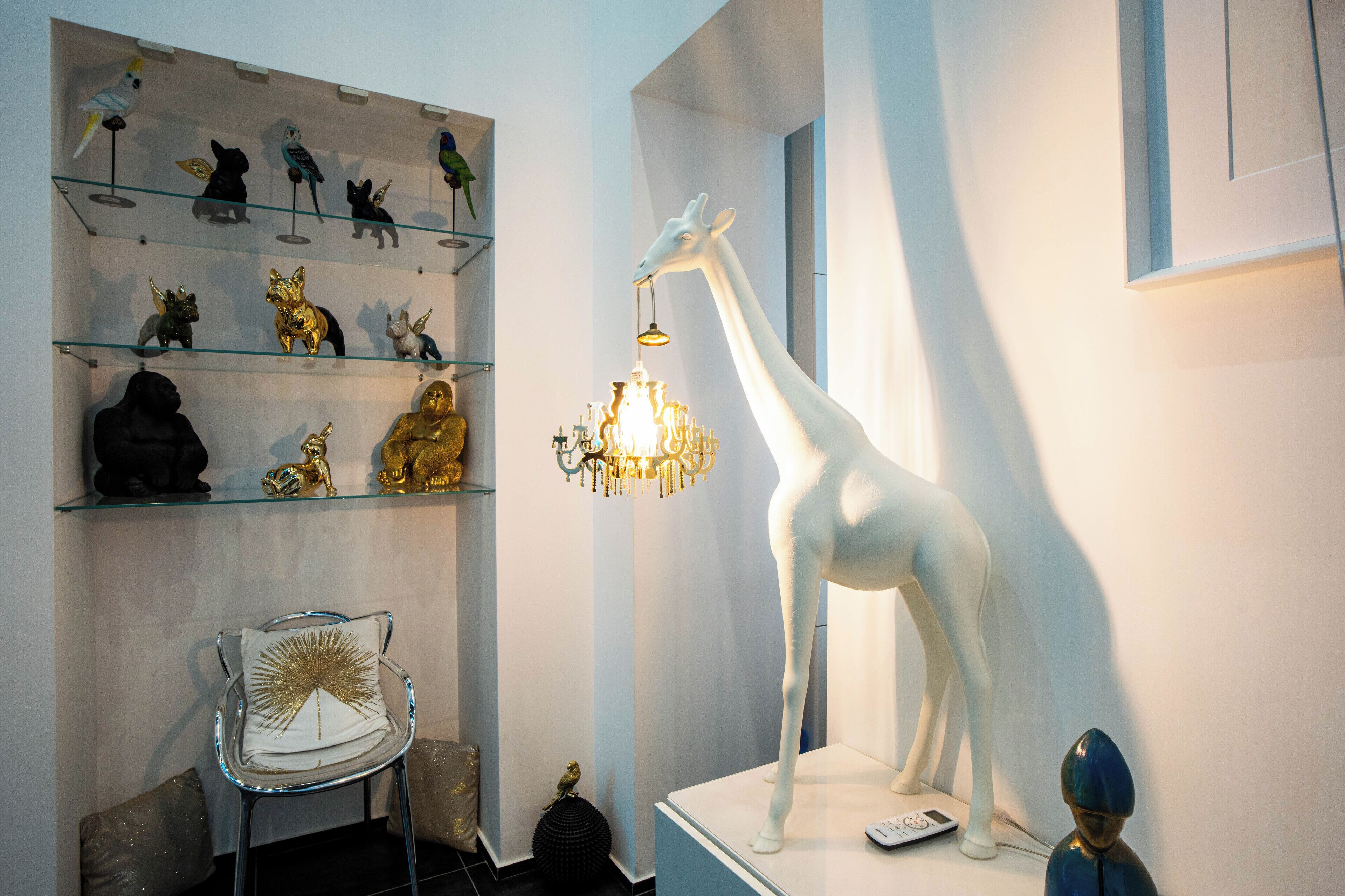 A room with a white giraffe sculpture, a chandelier, and various animal figurines on shelves.