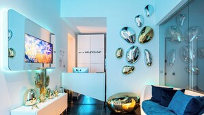 Una moderna hall d'albergo con una reception, un grande schermo televisivo e un'area relax con un divano blu.