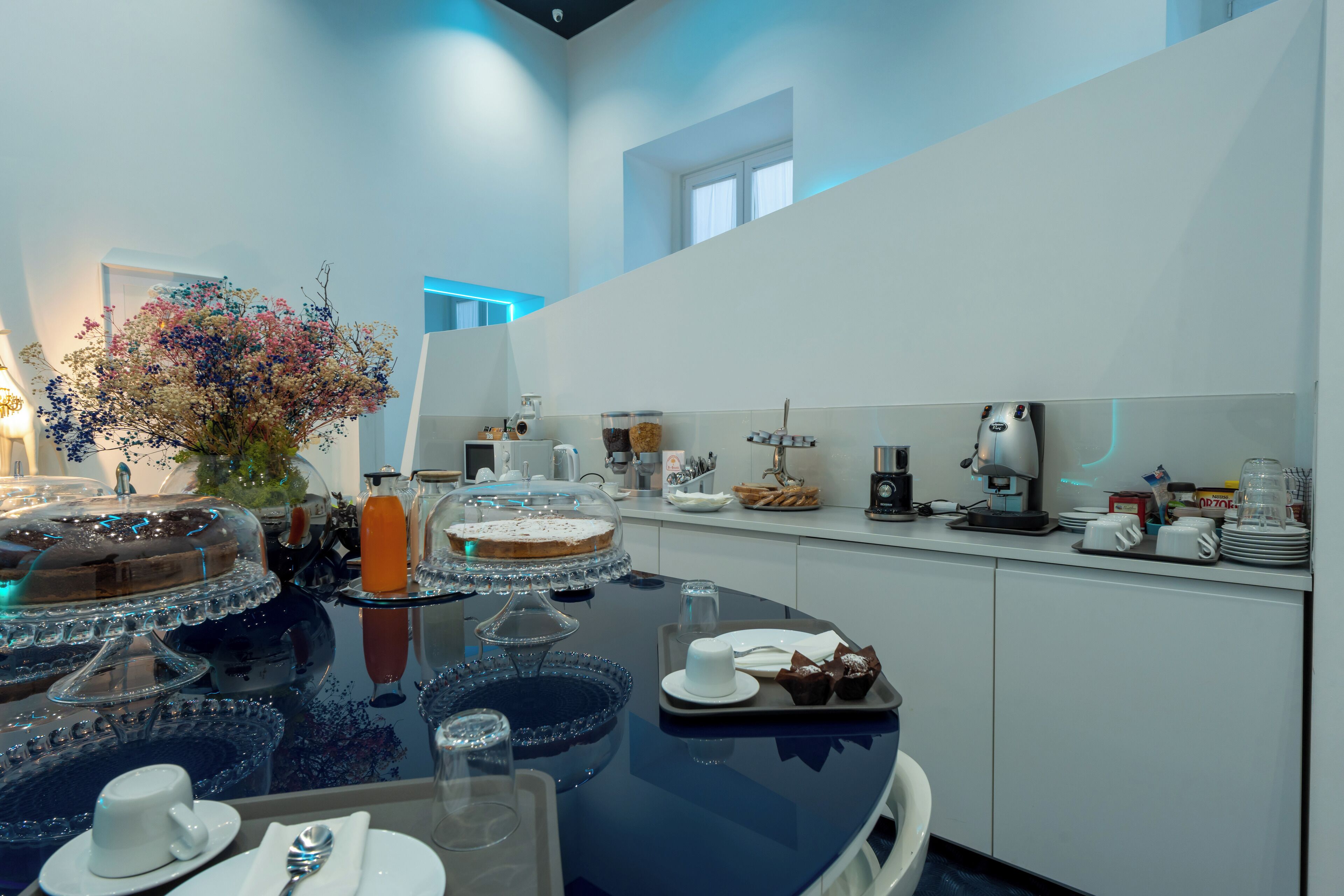 A modern kitchen with a round dining table, glassware, and a variety of food items.