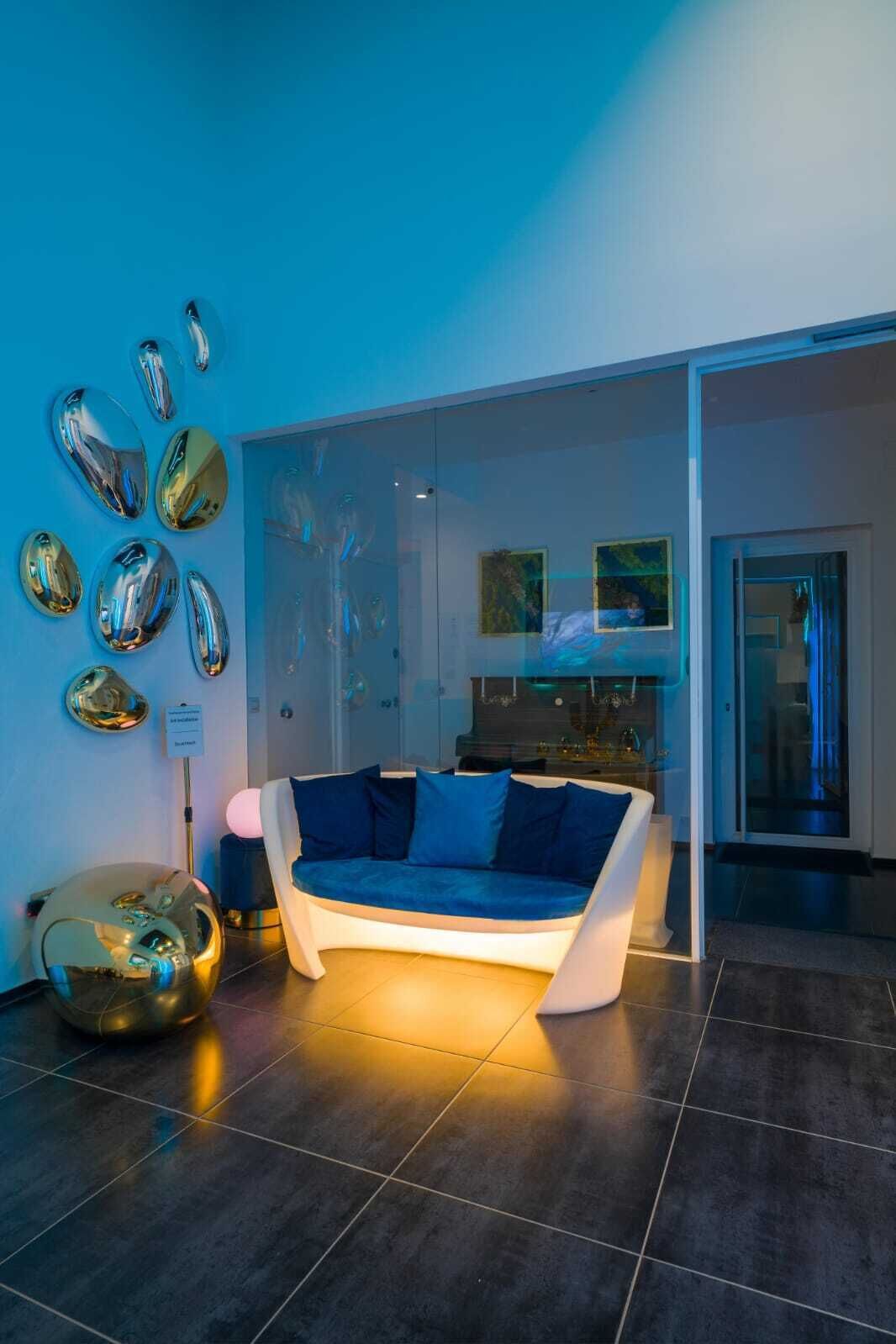 Een moderne woonkamer met een blauwe bank, een glazen wand en een bijzondere bolvormige sculptuur.
