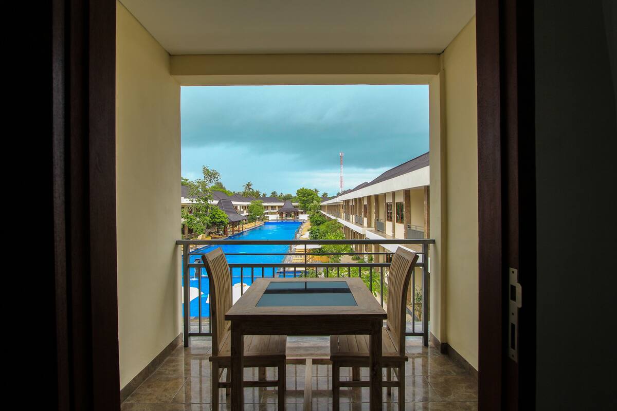 A balcony with a view of a swimming pool, a table, and chairs.