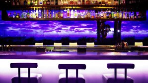 Un bar amb diverses estanteries plenes de botelles, un birretó i tres tamborets.