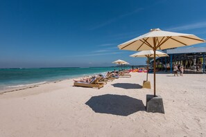 Una spiaggia con lettini e ombrelloni, cielo sereno e l'oceano sullo sfondo.