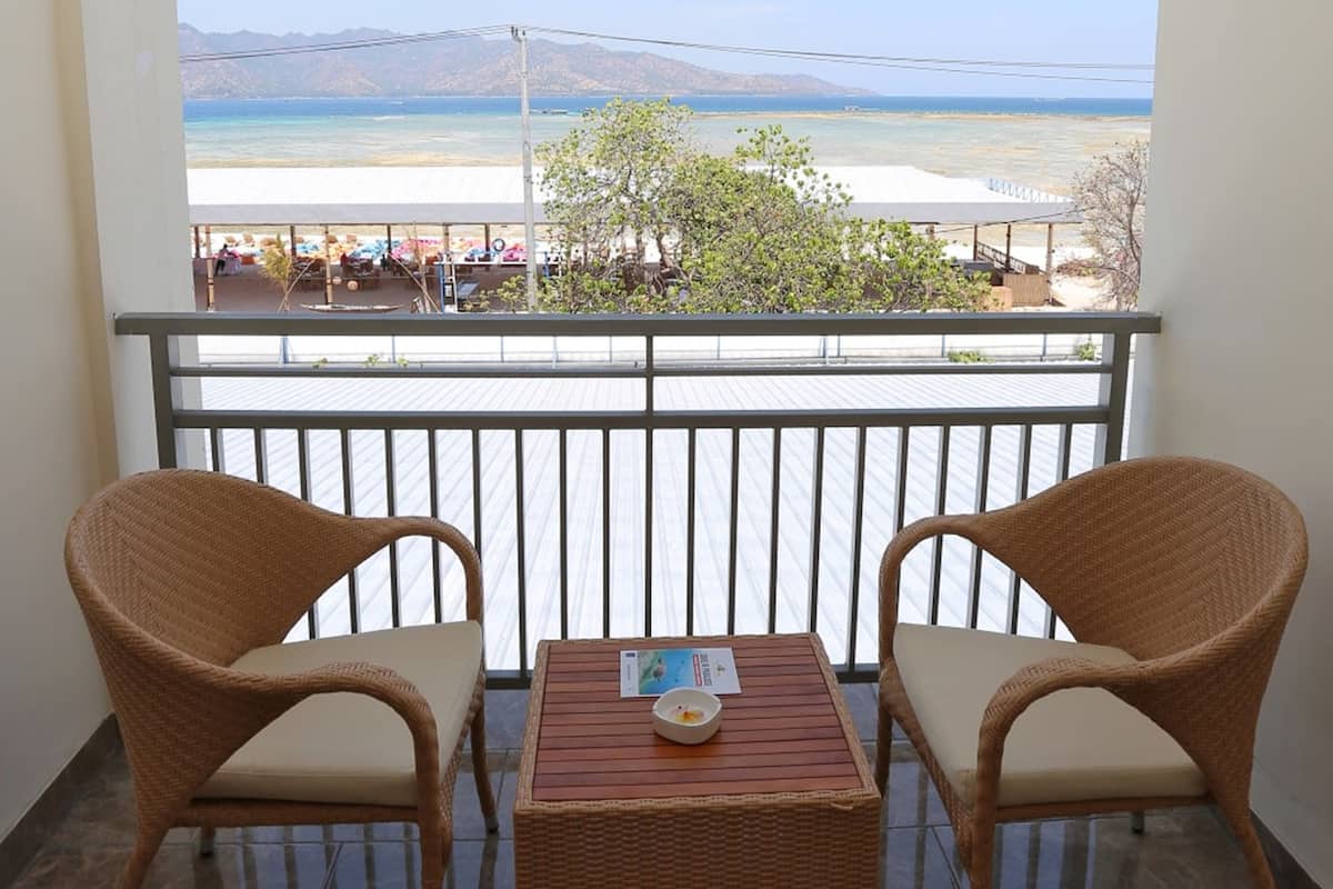 A balcony with wicker chairs and a small table, overlooking a beach and ocean.