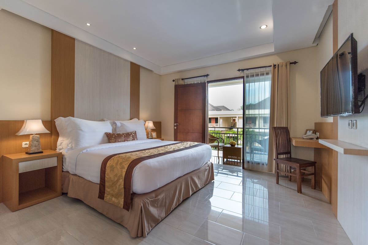 A hotel room with a large bed, a desk, a chair, and a TV mounted on the wall.