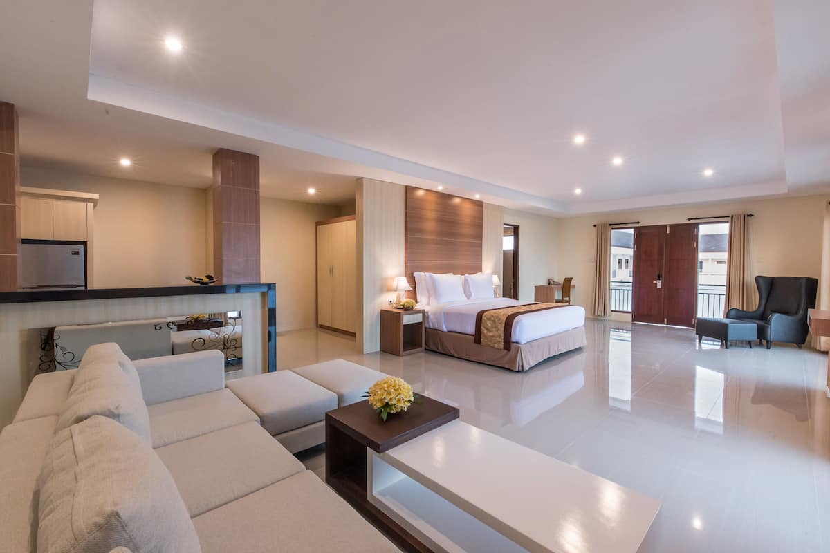 A modern hotel room with a large bed, a sofa, a small table with a flower, a desk, and a wardrobe.