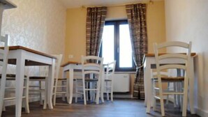 Une pièce comprenant une table à manger et quatre chaises, une fenêtre avec des rideaux et un radiateur.