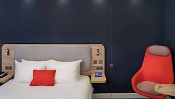 Una habitación de hotel con una cama, una silla roja y un panel de control en la pared.