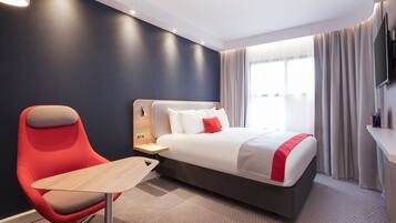 A modern hotel room with a large bed, a red chair, a small table, and a TV mounted on the wall.