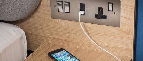 Un teléfono inteligente conectado a un enchufe con un cable USB sobre una mesita de noche de madera.