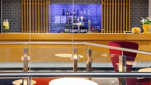 A modern bar area with a wooden counter, a variety of liquor bottles, and a red chair. - Holiday Inn Express Birmingham - City Centre by IHG (Birmingham)