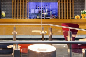A modern bar area with a wooden counter, a variety of liquor bottles, and a red chair. - Holiday Inn Express Birmingham - City Centre by IHG (Birmingham)