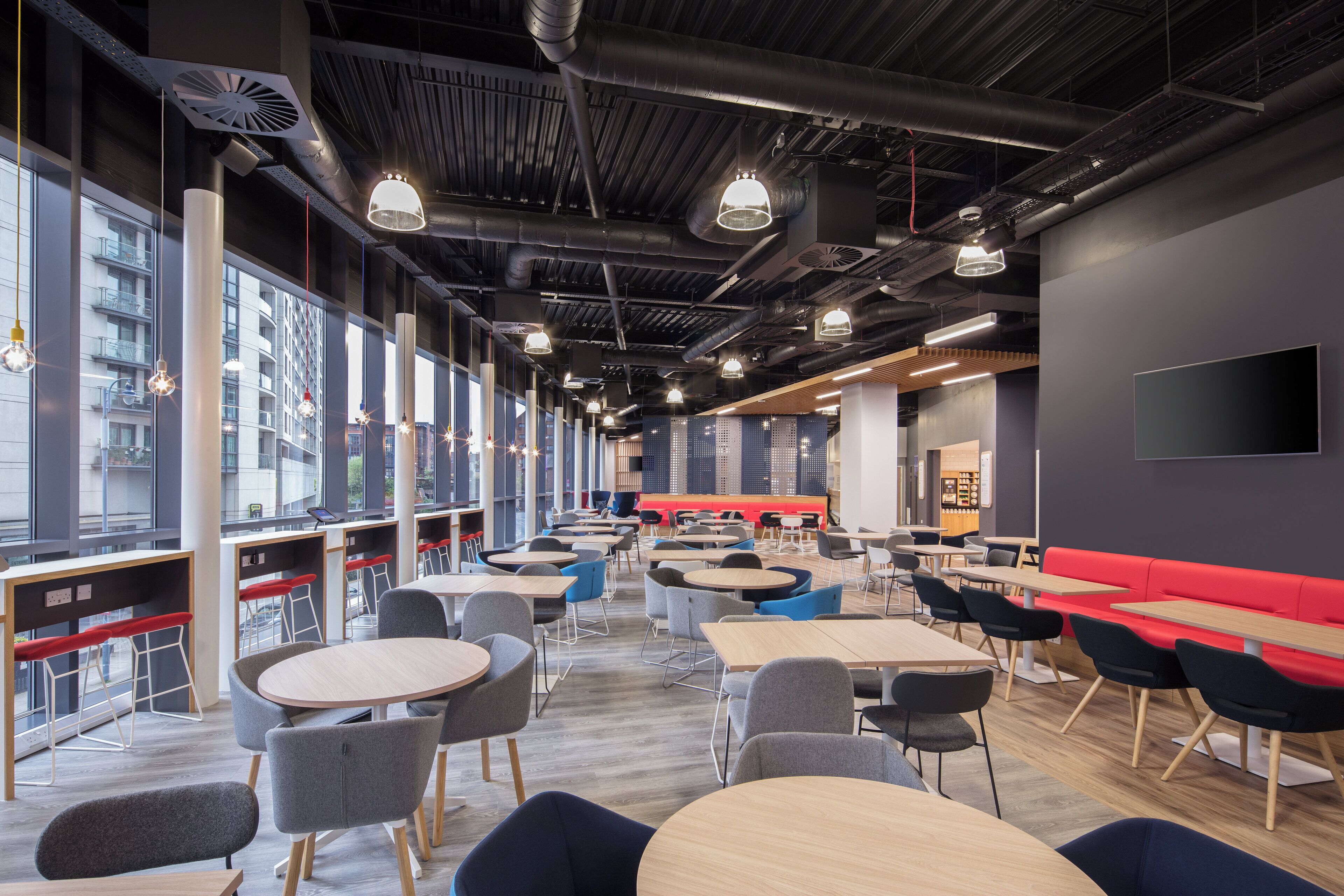 A modern interior with round tables and chairs, large windows, and a red seating area.