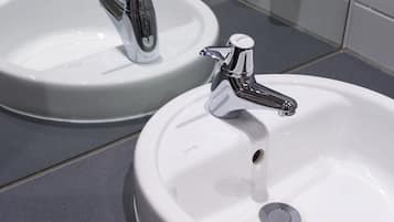 Two white bathroom sinks with chrome faucets, one labeled "VITA" and the other "SHIELD".
