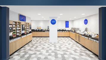 A modern cafe with a hexagonal patterned floor, coffee machines, and a variety of breakfast items.