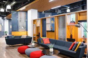 A modern lounge area with sofas, ottomans, and a coffee table. - Holiday Inn Express Birmingham - City Centre by IHG (Birmingham)
