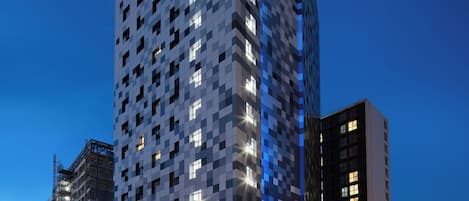 Un hotel de varios pisos con fachada moderna, un letrero de Holiday Inn Express y una calle concurrida con vehículos en movimiento.