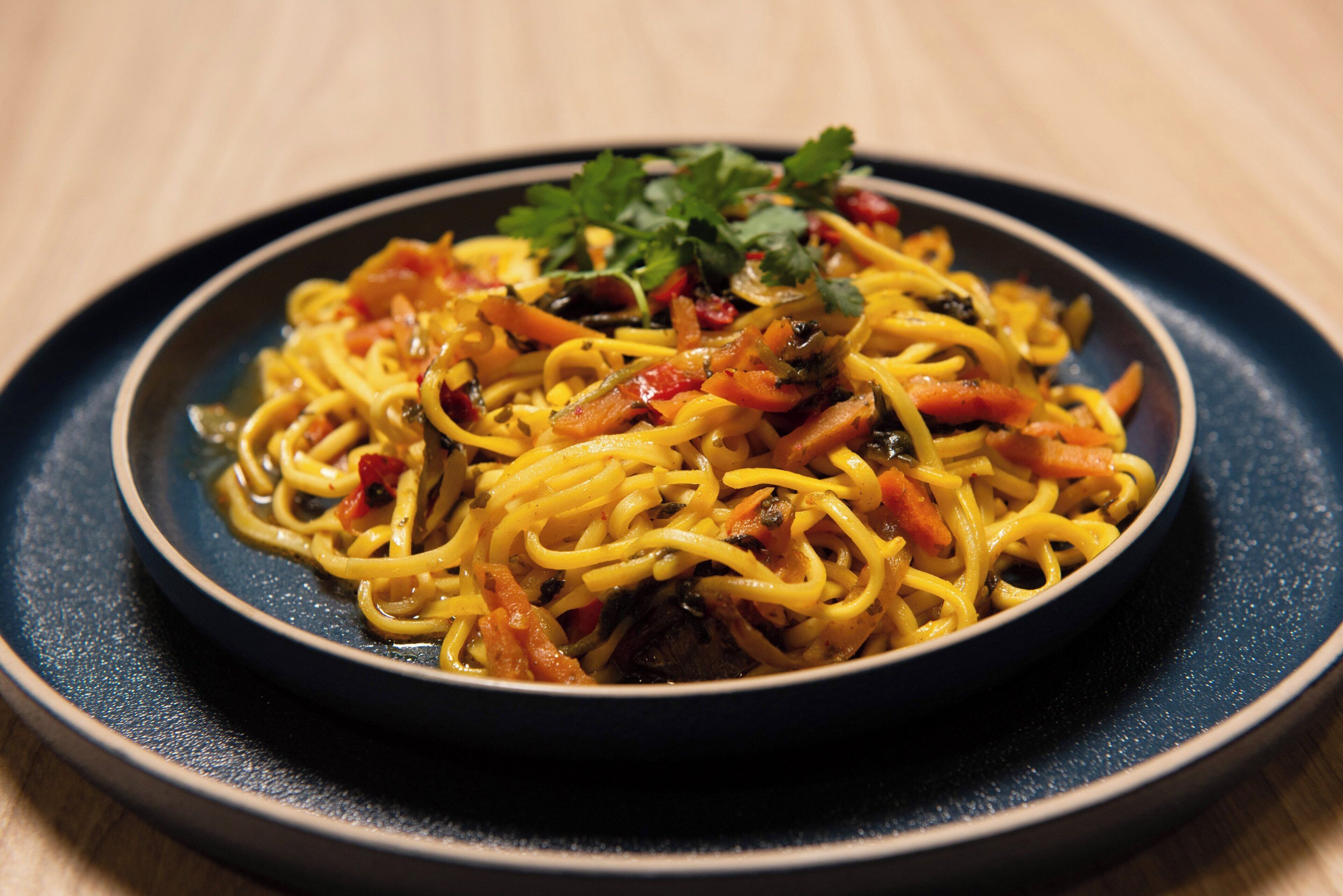 Une assiette de spaghettis aux légumes, agrémentée d’une garniture, le tout présenté sur une assiette foncée.