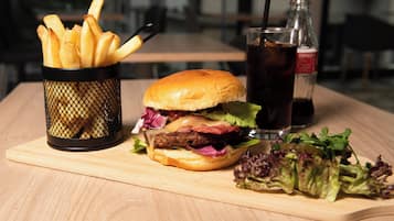 A meal consisting of a burger, fries, a salad, and a drink on a wooden table.