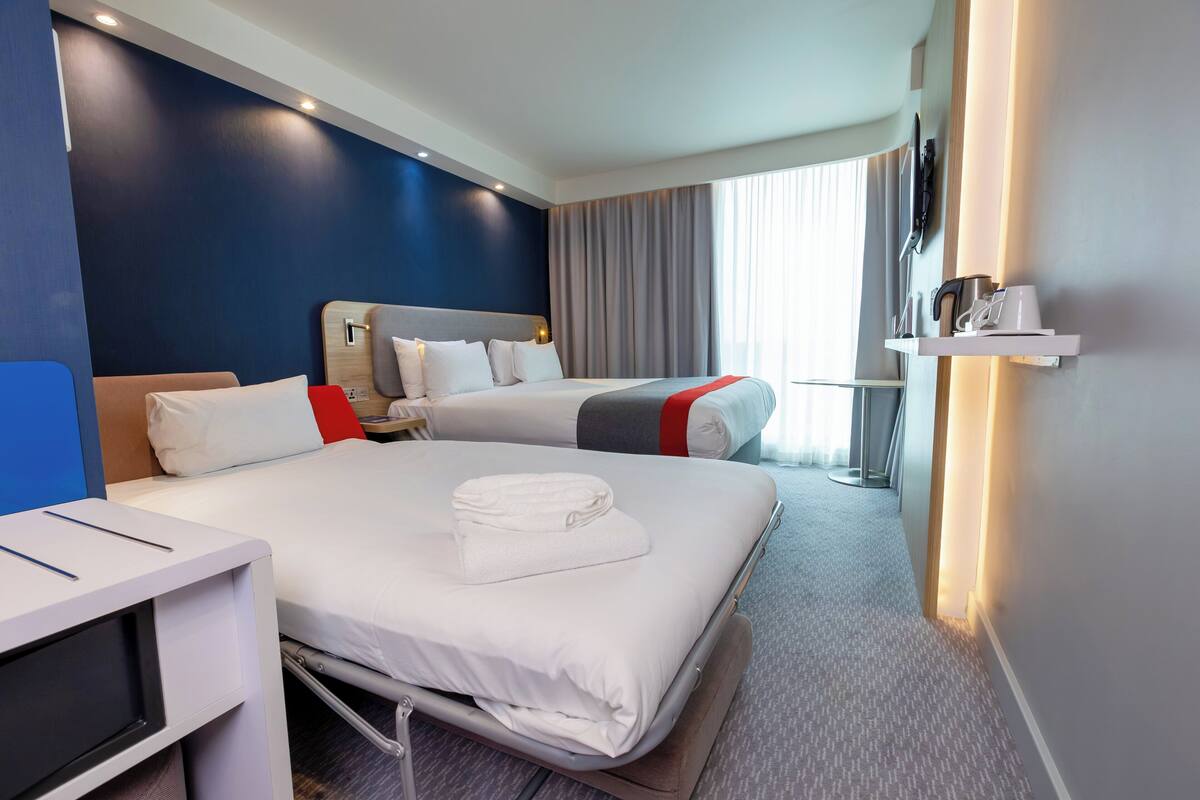 Een hotelkamer met twee bedden, een bureau, een televisie en een raam met gordijnen.
