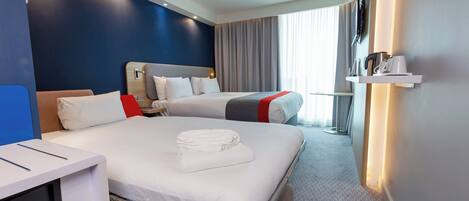 A hotel room with two beds, a desk, a TV, and a window with curtains.