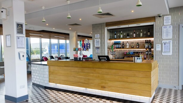 A hotel reception area with a wooden counter, tiled floor, and a bar with various bottles and glasses.
