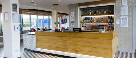 A hotel reception area with a wooden counter, tiled floor, and a bar with various bottles and glasses.