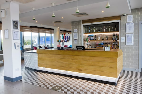 A hotel reception area with a wooden counter, tiled floor, and a bar with various bottles and glasses. - Holiday Inn Express Manchester - Trafford City by IHG (Manchester)