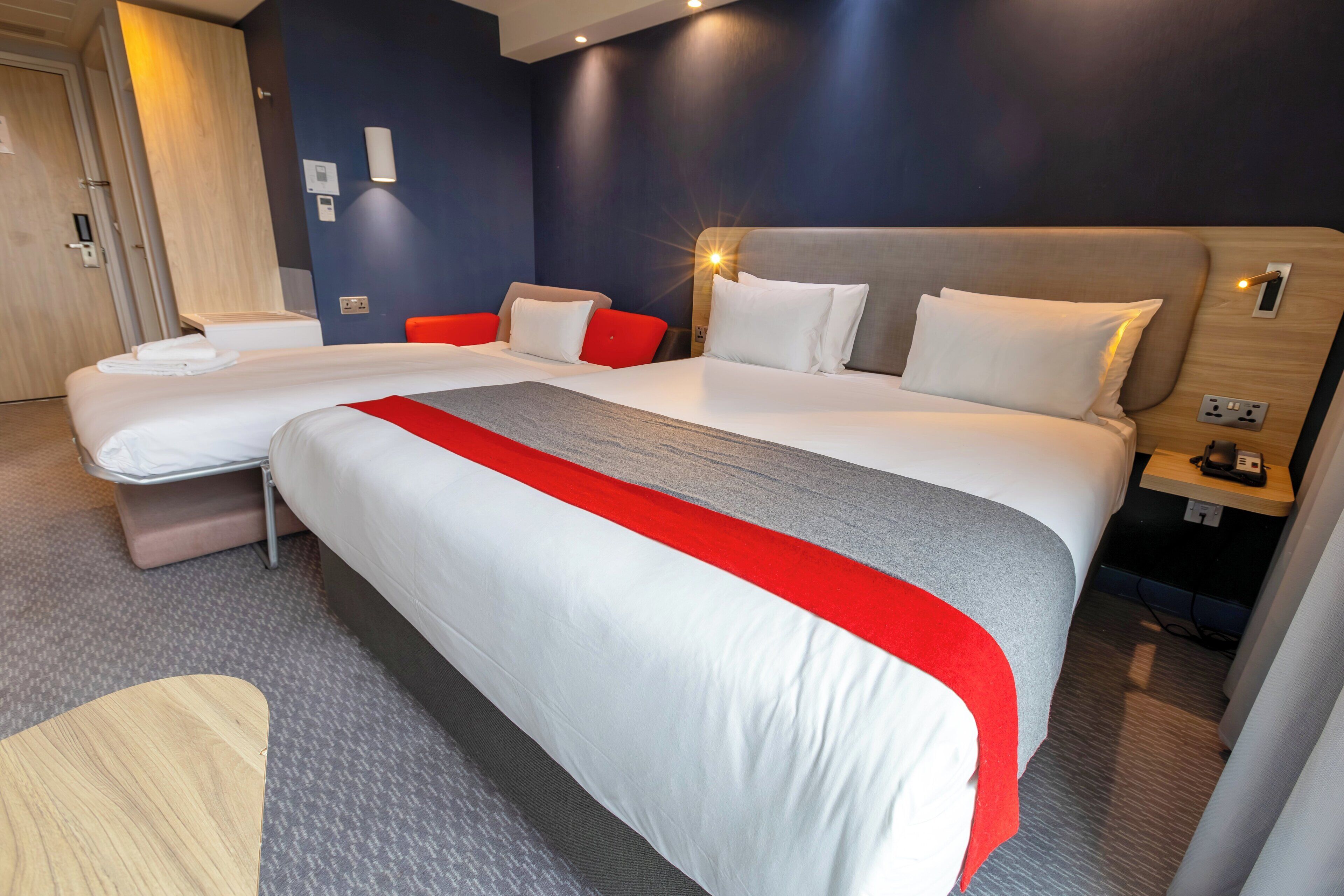 A hotel room with two beds, a wooden nightstand, and a red accent wall.