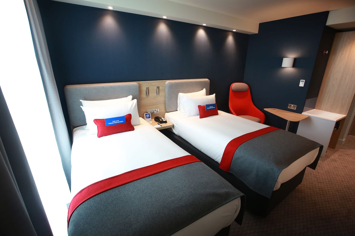Een hotelkamer met twee bedden, een rode stoel, een kleine tafel en een nachtkastje.