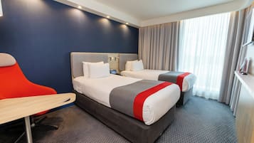 A hotel room with two beds, a desk, and a chair.