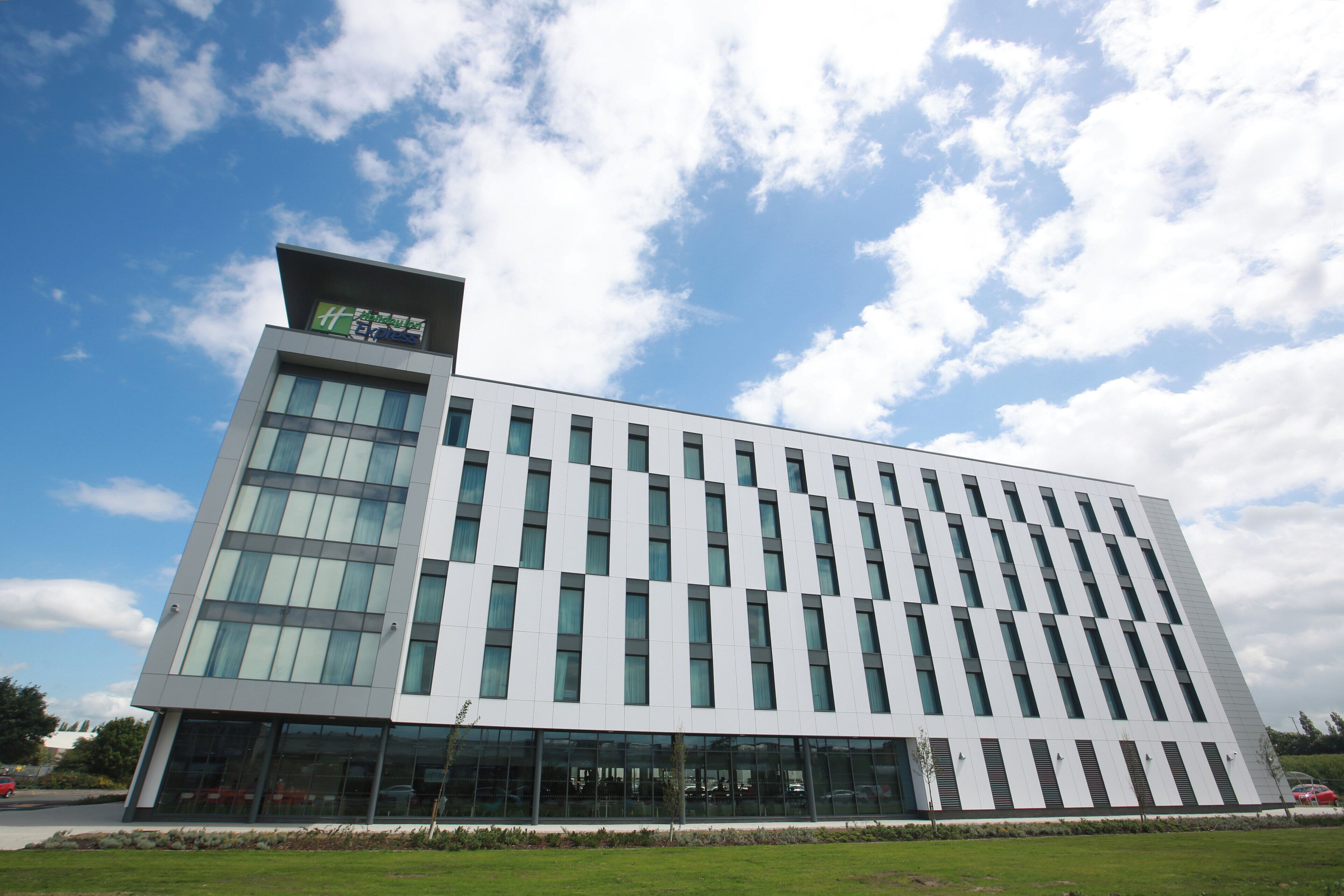 A modern hotel building with a flat roof, large windows, and a clear sky with clouds.