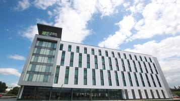 A modern hotel building with a flat roof, large windows, and a clear sky with clouds.