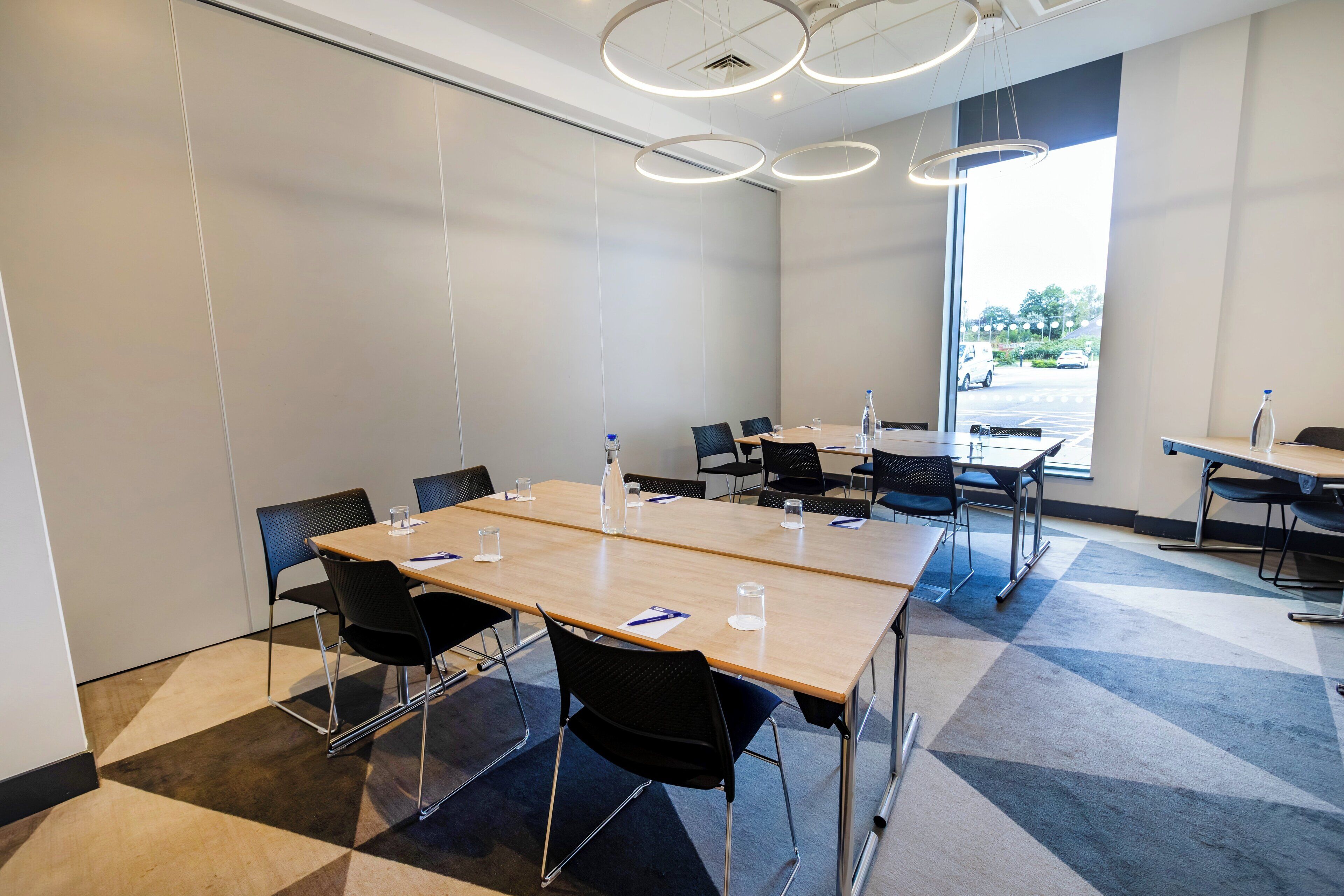 Une salle de conférence dotée d’une grande table, de chaises et offrant une vue sur un parking grâce à une grande fenêtre.