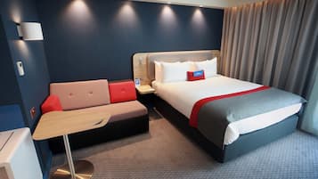 A hotel room with a bed, a sofa, a desk, and a lamp.