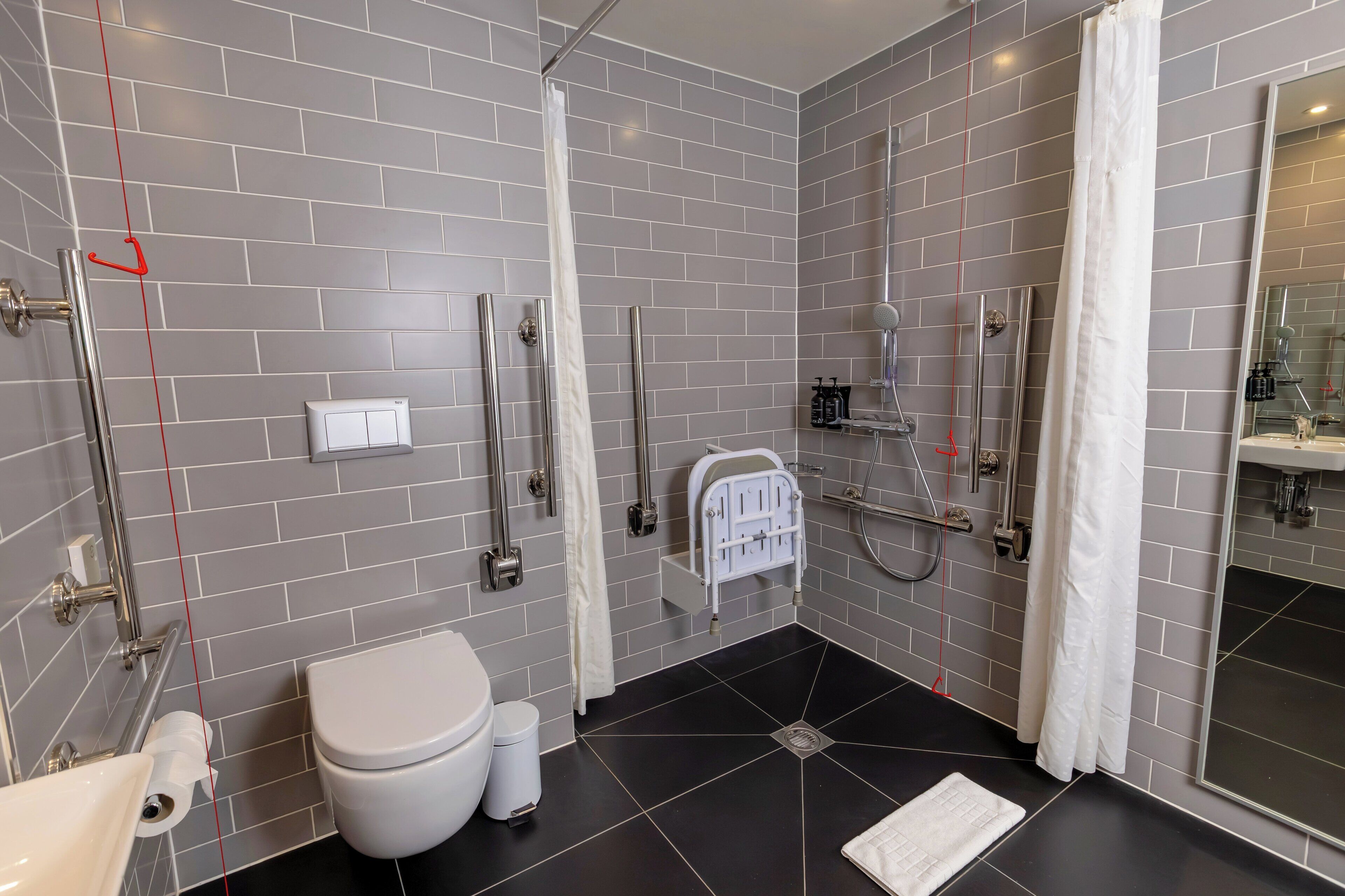 Et moderne badeværelse med grå flisevægge, et hvidt toilet, en vask og et bruseområde.