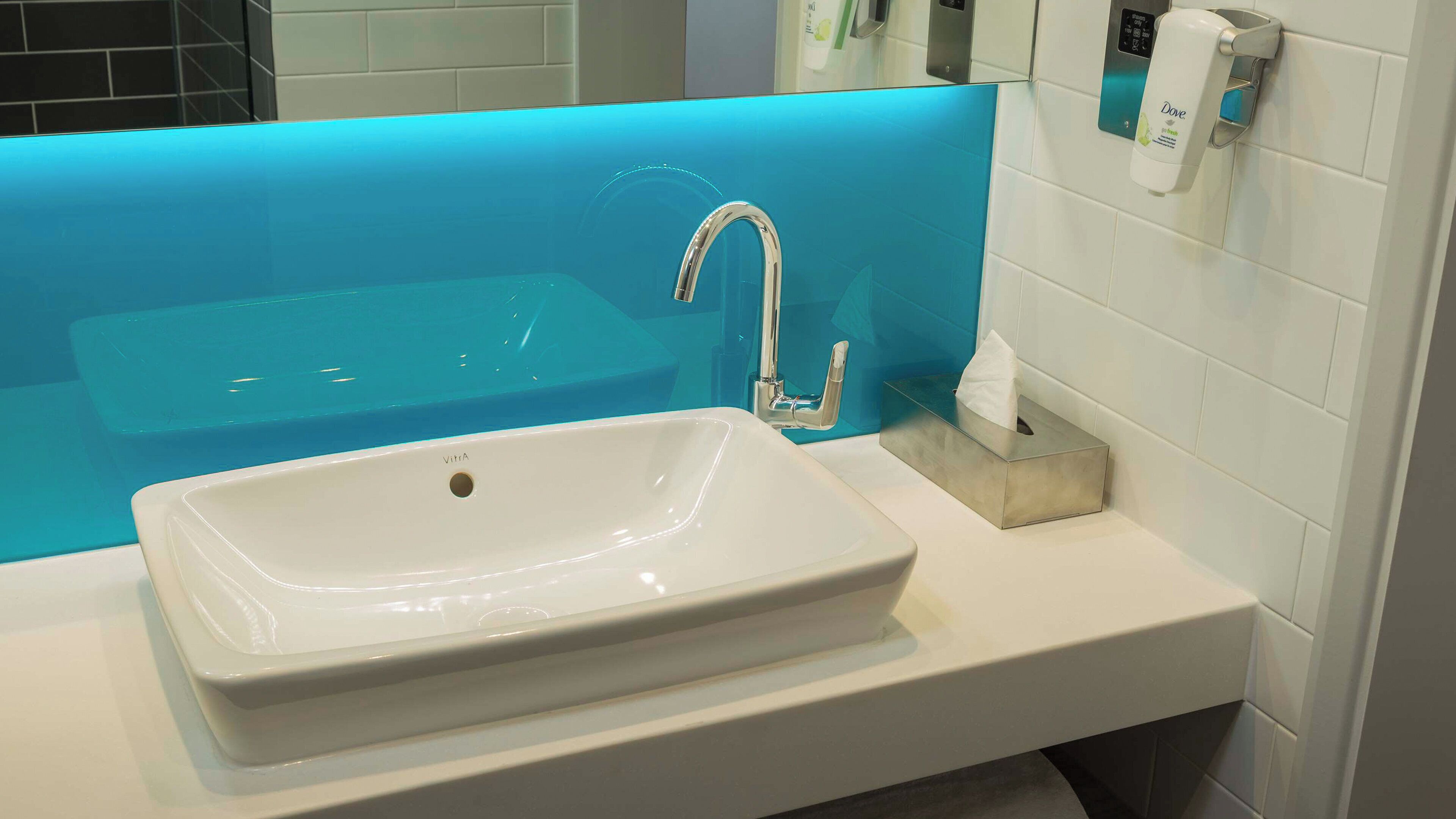 A bathroom with a white sink, a blue accent wall, and a soap dispenser.