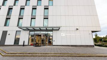 Una entrada moderna de hotel con puerta de vidrio, zona de acceso cubierta y cartel que indica que es el Holiday Inn Express en Manchester y Trafford City.