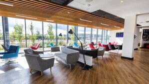 A modern lounge area with a variety of seating options, large windows offering a view of the outdoors, and a contemporary design with wooden slats on the ceiling.