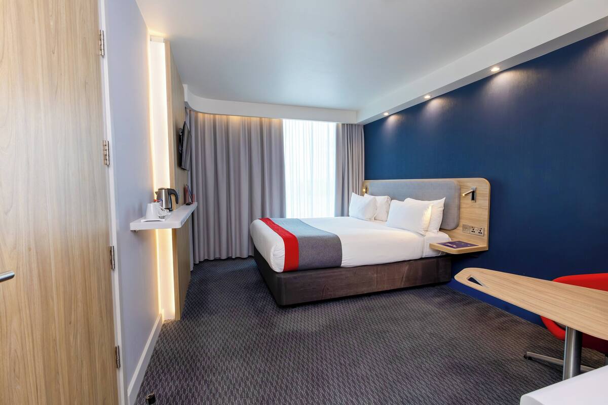 Een moderne hotelkamer met een groot bed, een bureau en een aan de muur bevestigde televisie.