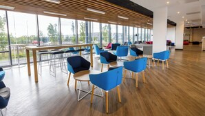 A modern conference room with large windows, wooden slats on the ceiling, and blue chairs around a central table.