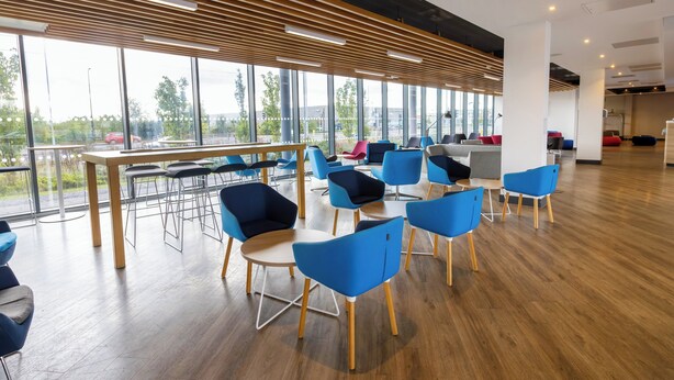 Une salle de conférence moderne, dotée de grandes fenêtres, de lambris en bois au plafond et de chaises bleues disposées autour d’une table centrale.