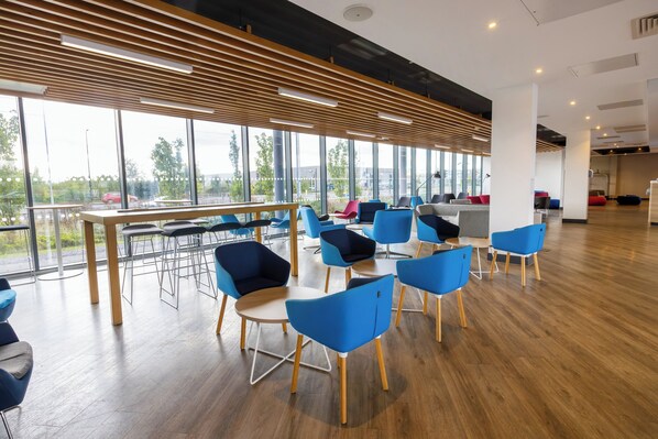 A modern conference room with large windows, wooden slats on the ceiling, and blue chairs around a central table. - Holiday Inn Express Manchester - Trafford City by IHG (Manchester)