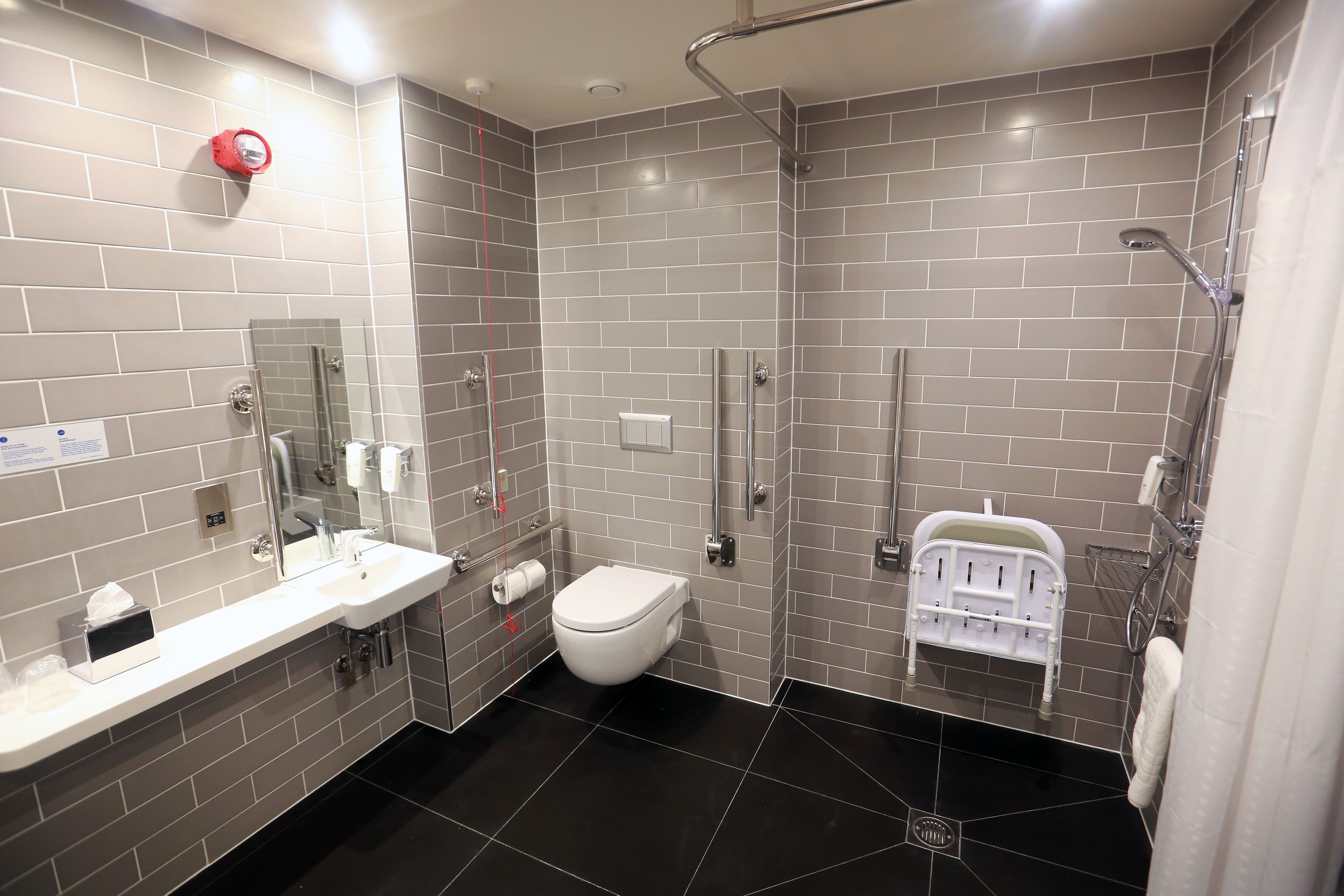 A modern bathroom with grey tiled walls, a white sink, a toilet, and a shower area.