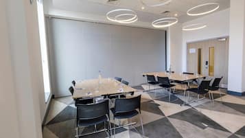 Una sala de conferències amb diverses taules i cadires, finestres grans i un disseny de sostre modern.