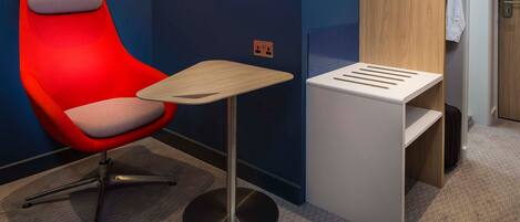 Una habitación de hotel moderna con una silla roja, una mesita de madera y un mueble blanco con estantes.