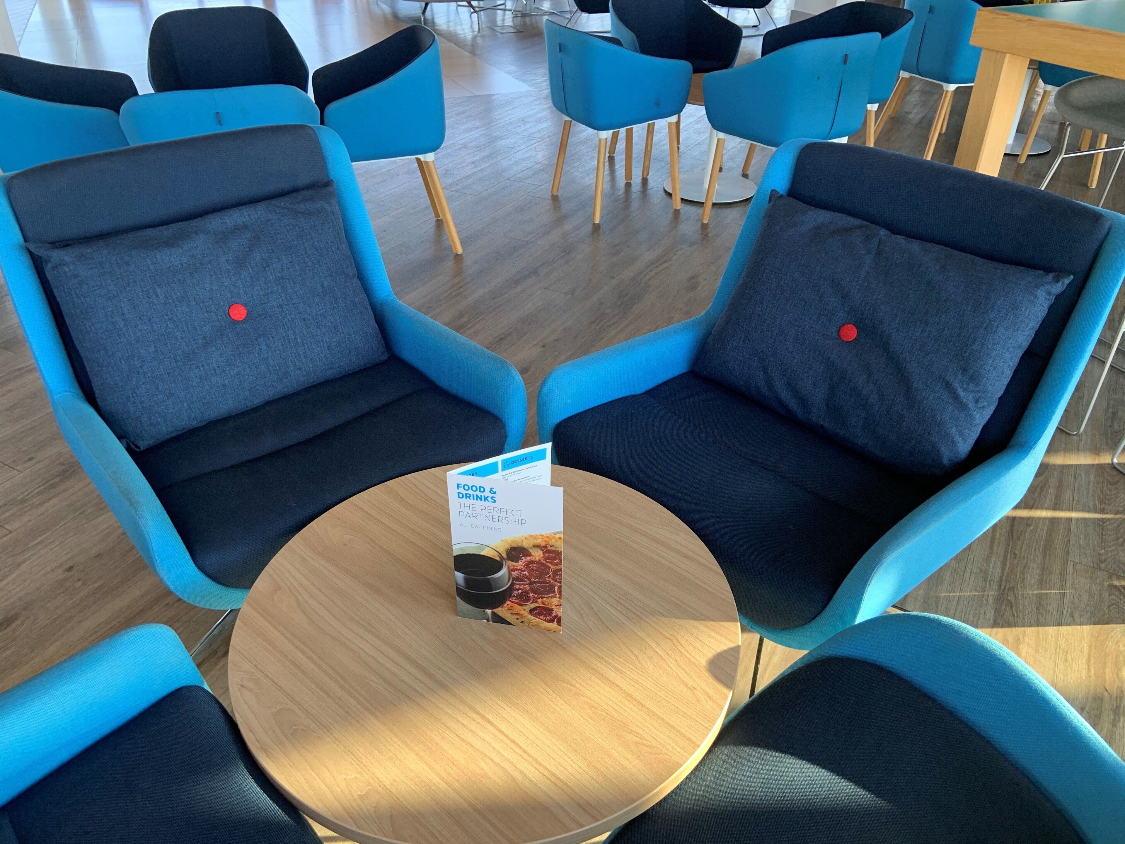 Une table ronde avec un menu placé au centre, entourée de chaises bleues dotées de coussins noirs.