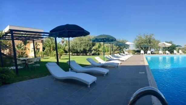 A swimming pool with lounge chairs and umbrellas, surrounded by greenery and a clear sky. - Zaiera Resort Club (Solarino)
