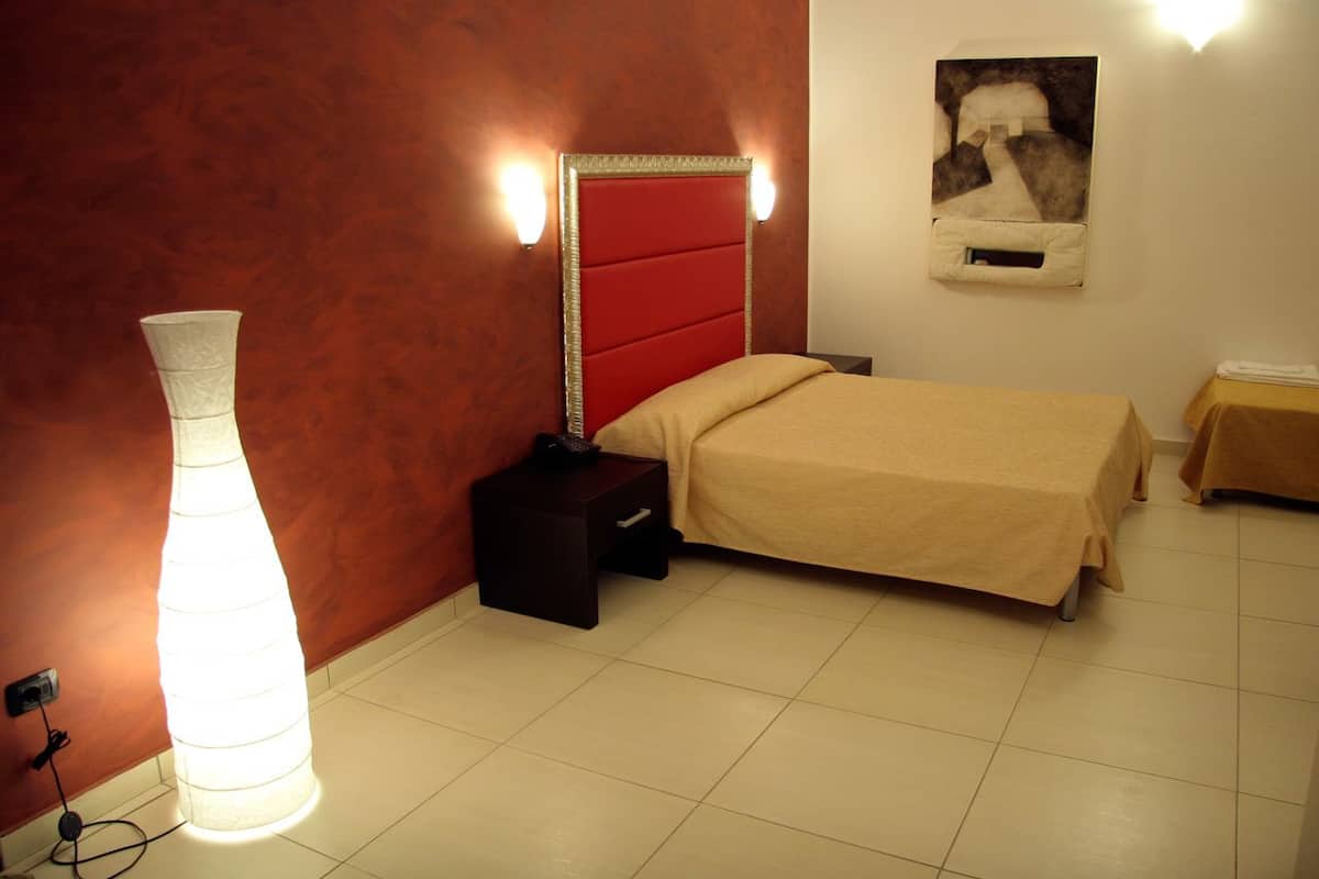 A hotel room with a bed, bedside table, lamp, and a wall-mounted artwork.