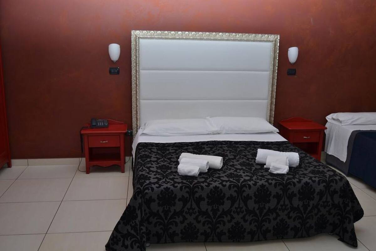 A hotel room with a large bed, two bedside tables, and a red wall.